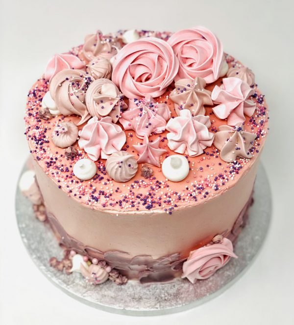 Handmade bespoke pink celebration cake with freshly baked pink meringue kisses and swirls