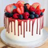 Stunning vanilla sponge cake with raspberry drip topped with fresh berries and fresh French macarons