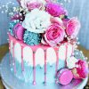 Gourmet pink birthday cake with drip detail with fresh pink and blue flowers and macaron topping