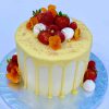 Handcrafted vanilla drip celebration cake with fresh strawberries, raspberries and decorative flowers